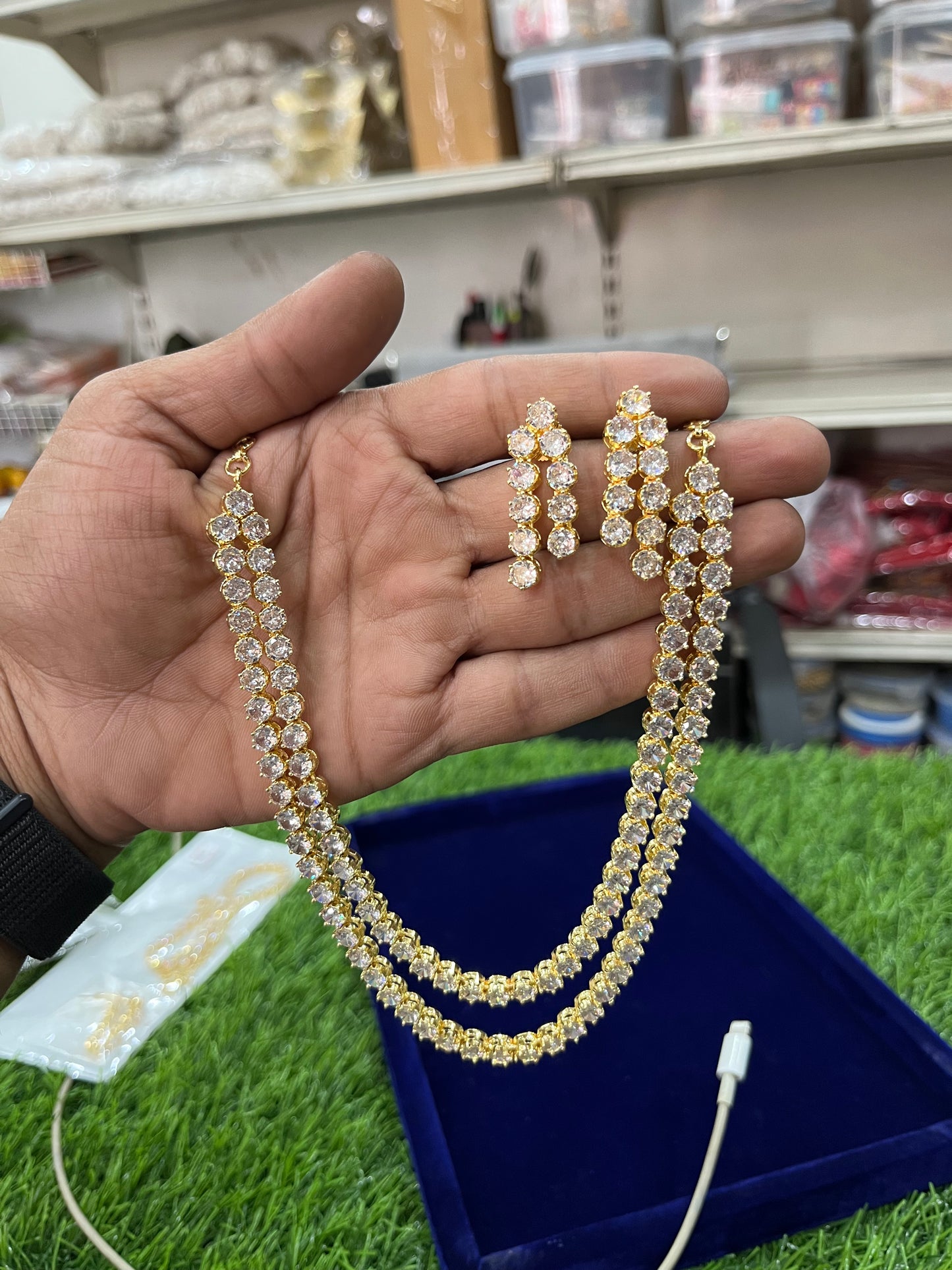Hand holding a set of gold american diamond necklace and earrings with a blurred store background