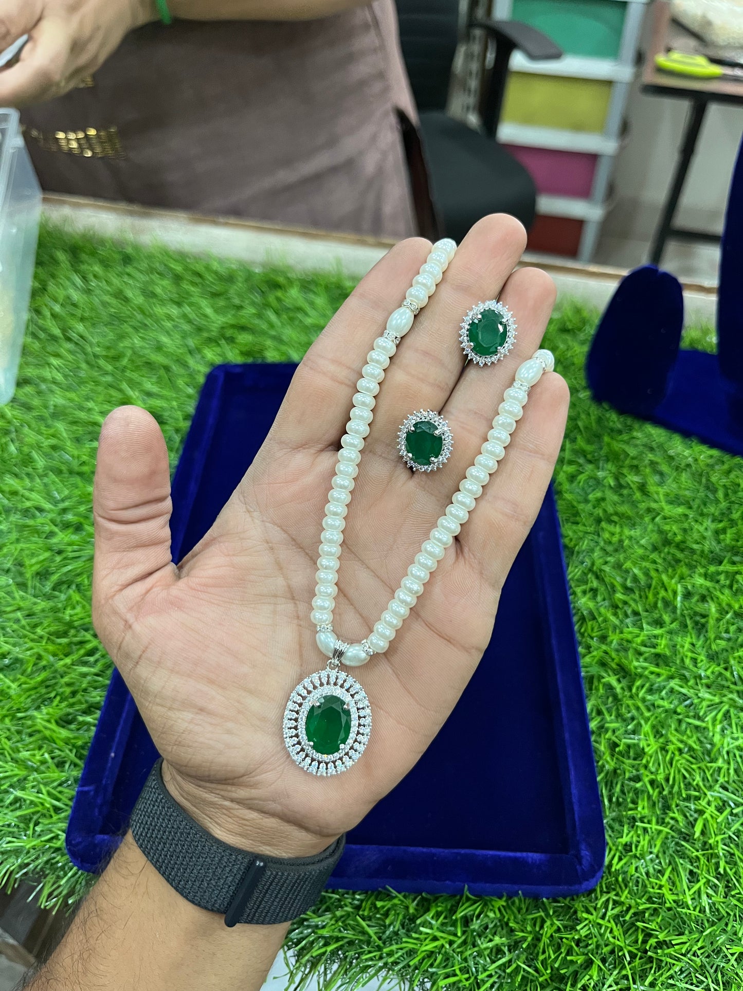 Hand holding a green emerald necklace and earrings on a grassy background