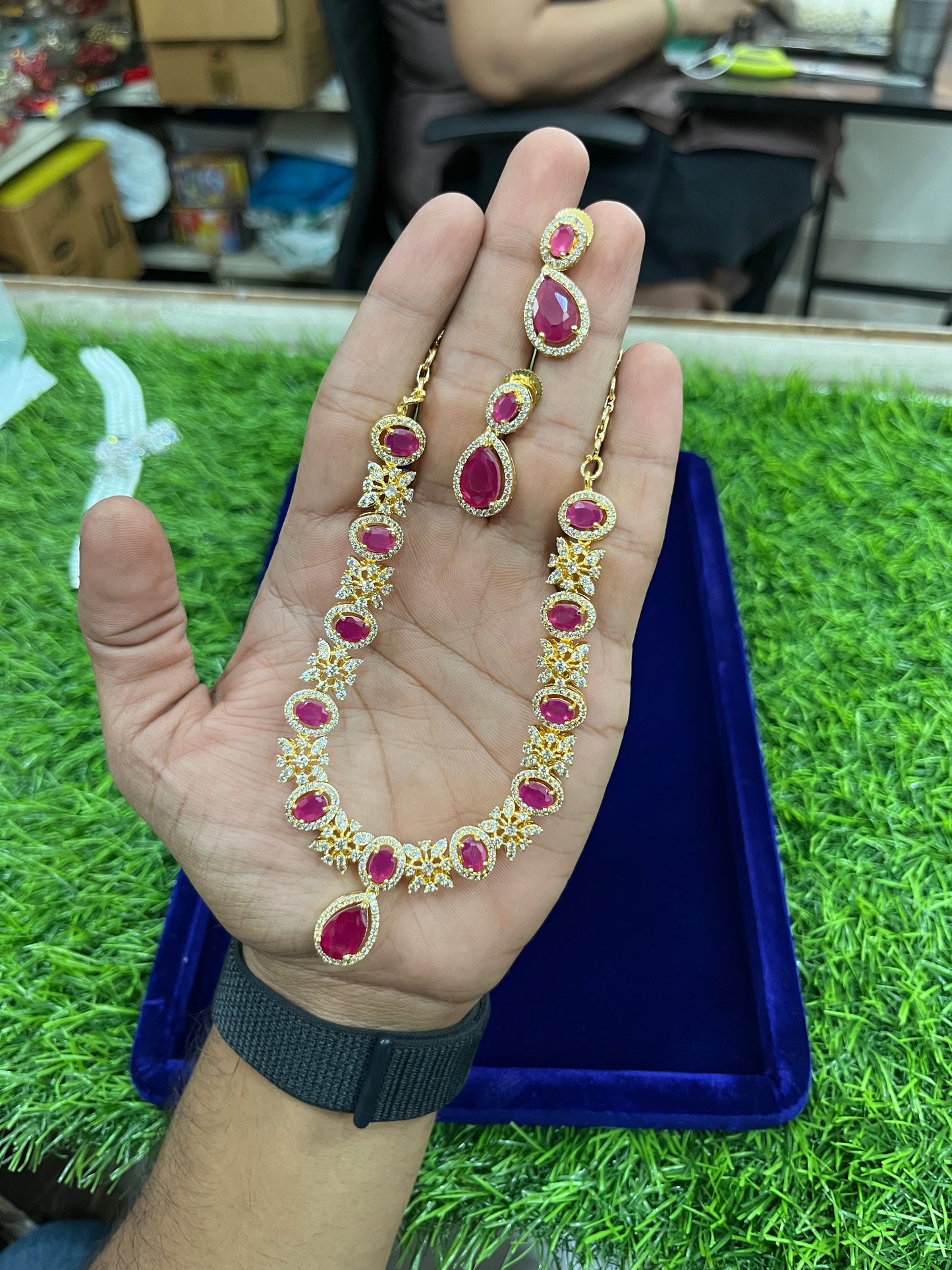 Gold necklace with red gemstones held in a hand on a grassy surface