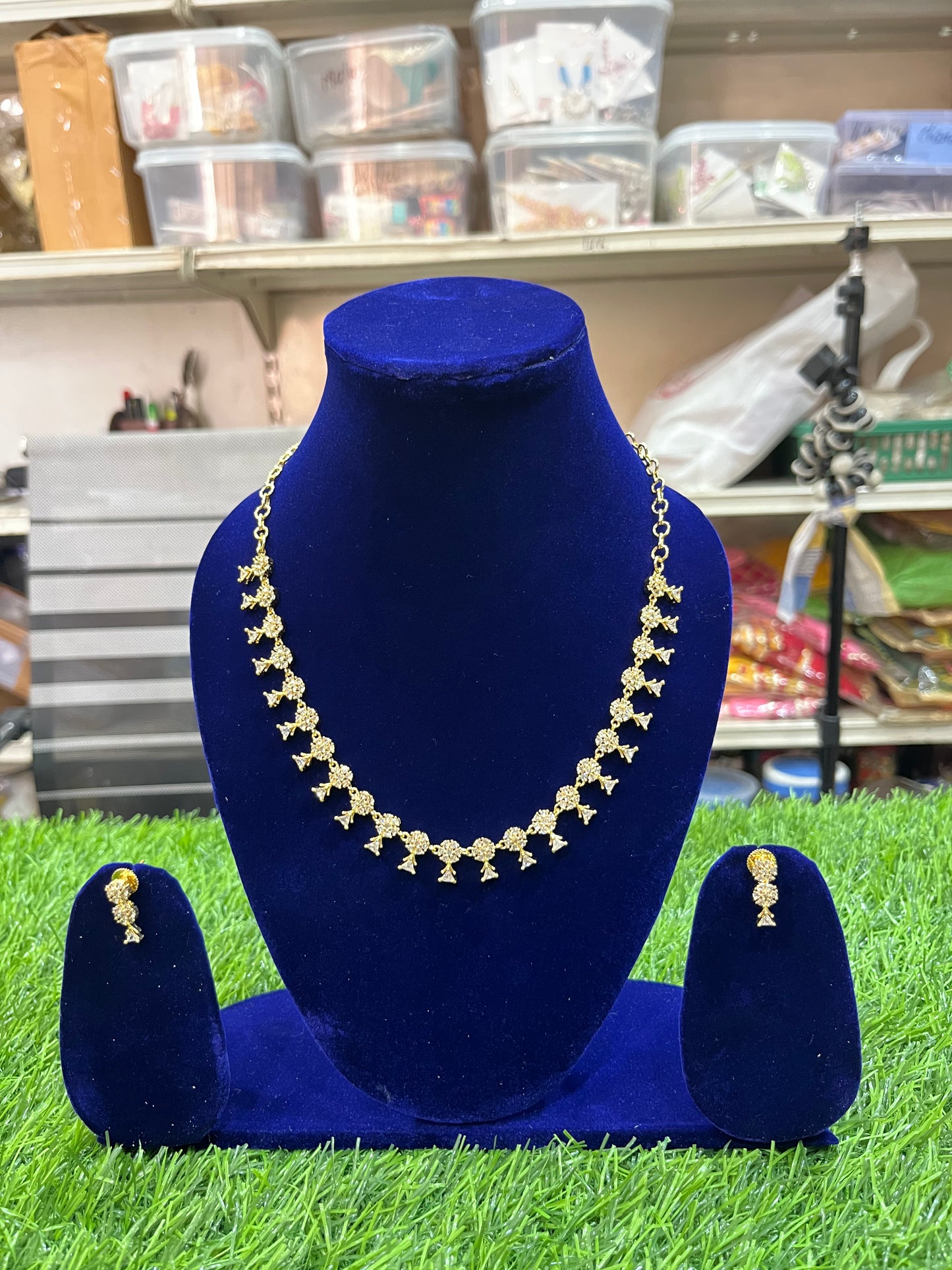 Necklace and earrings set on a blue velvet stand with a store shelf in the background