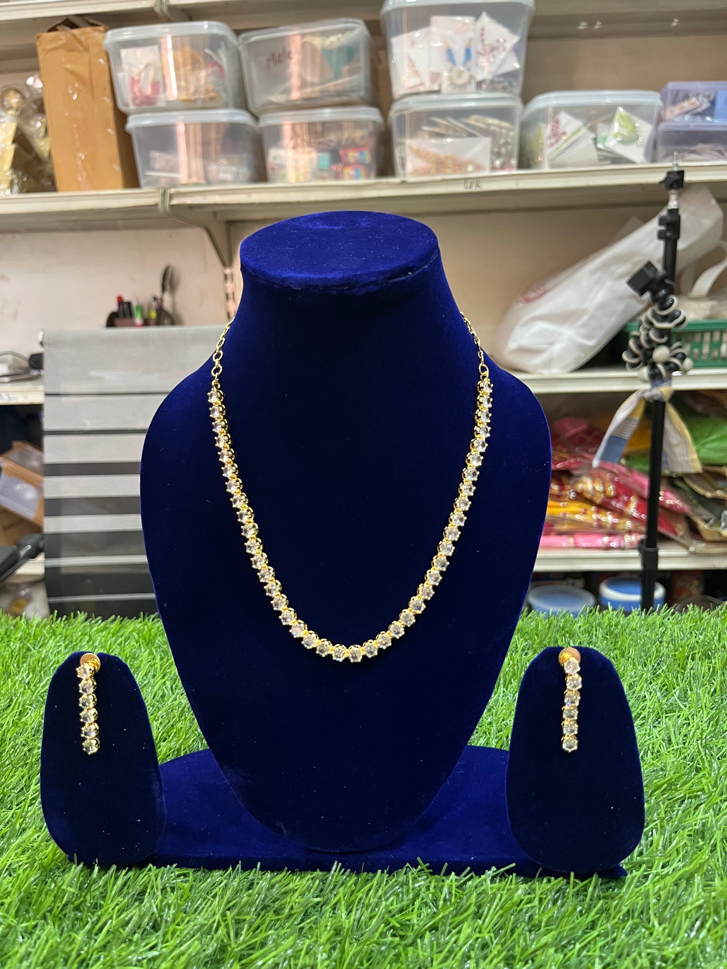 Gold necklace and earrings on a blue velvet stand with a cluttered background