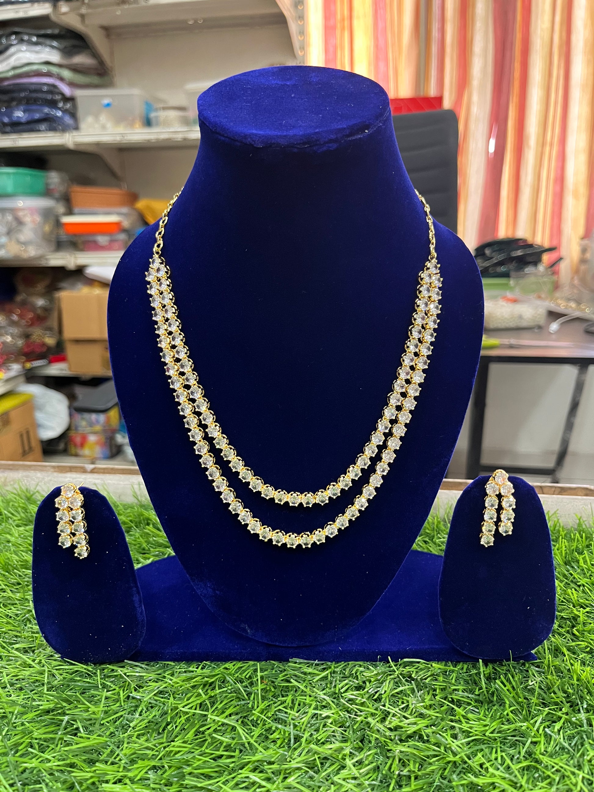 AD necklace and earrings on a blue velvet stand with a blurred indoor background